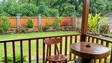 A wooden deck with a round table and two chairs, overlooking a garden with a wooden fence and various plants.