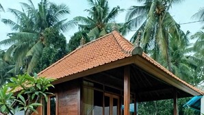 A wooden house with a tiled roof, a porch, and a small garden area with palm trees. - Borneo Log Cabin Guest House (Tejakula)