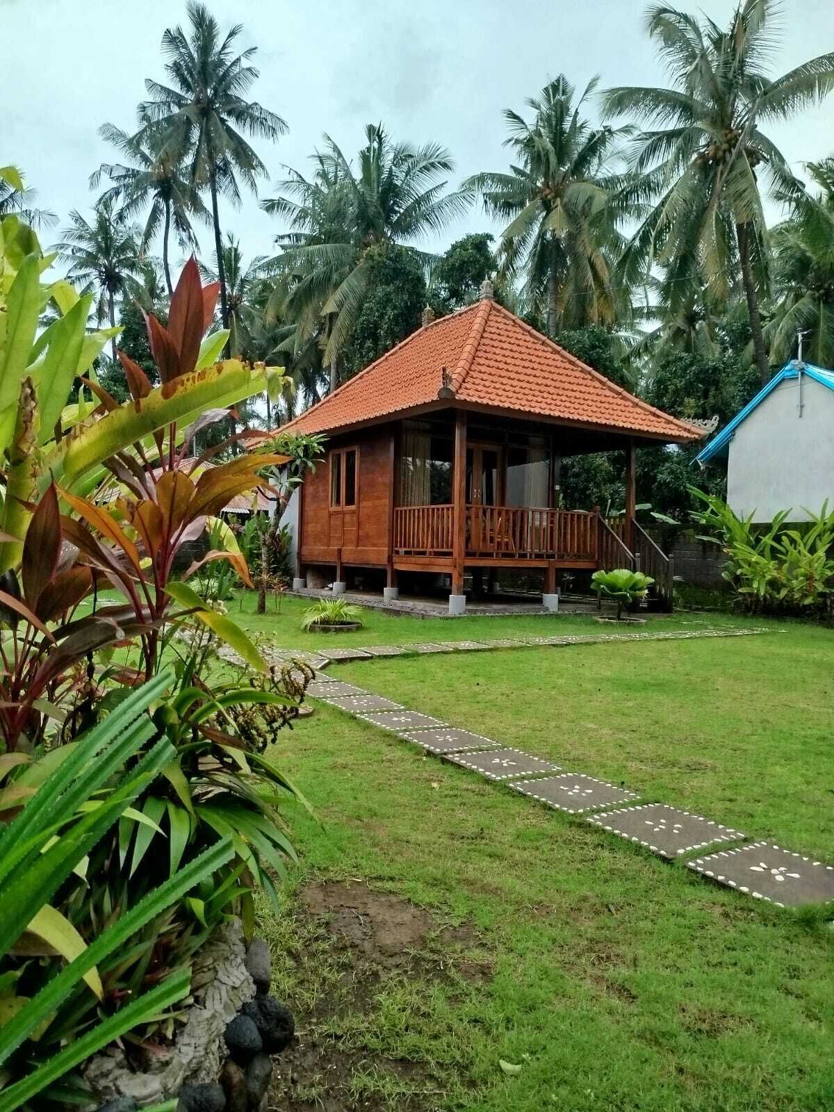A wooden house with a tiled roof, surrounded by a well-maintained lawn and palm trees.