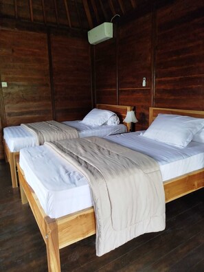 Una habitación de madera con dos camas individuales, una mesita de noche con lámpara y un aire acondicionado instalado en la pared.