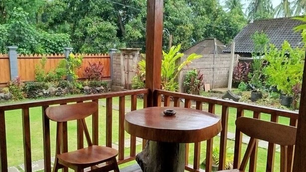 Un espacio al aire libre cubierto con una mesa y sillas de madera, rodeado por una valla de madera y abundante vegetación.
