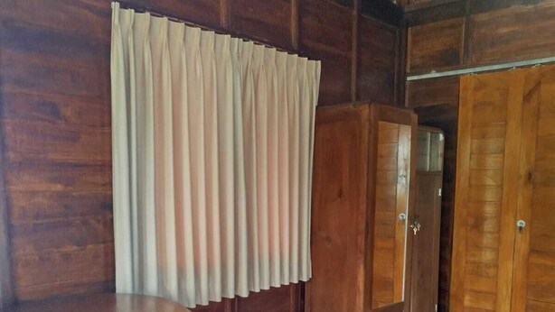A room with a wooden floor, a round wooden table, a bed with a striped blanket, and wooden wardrobes. - Borneo Log Cabin Guest House (Tejakula)