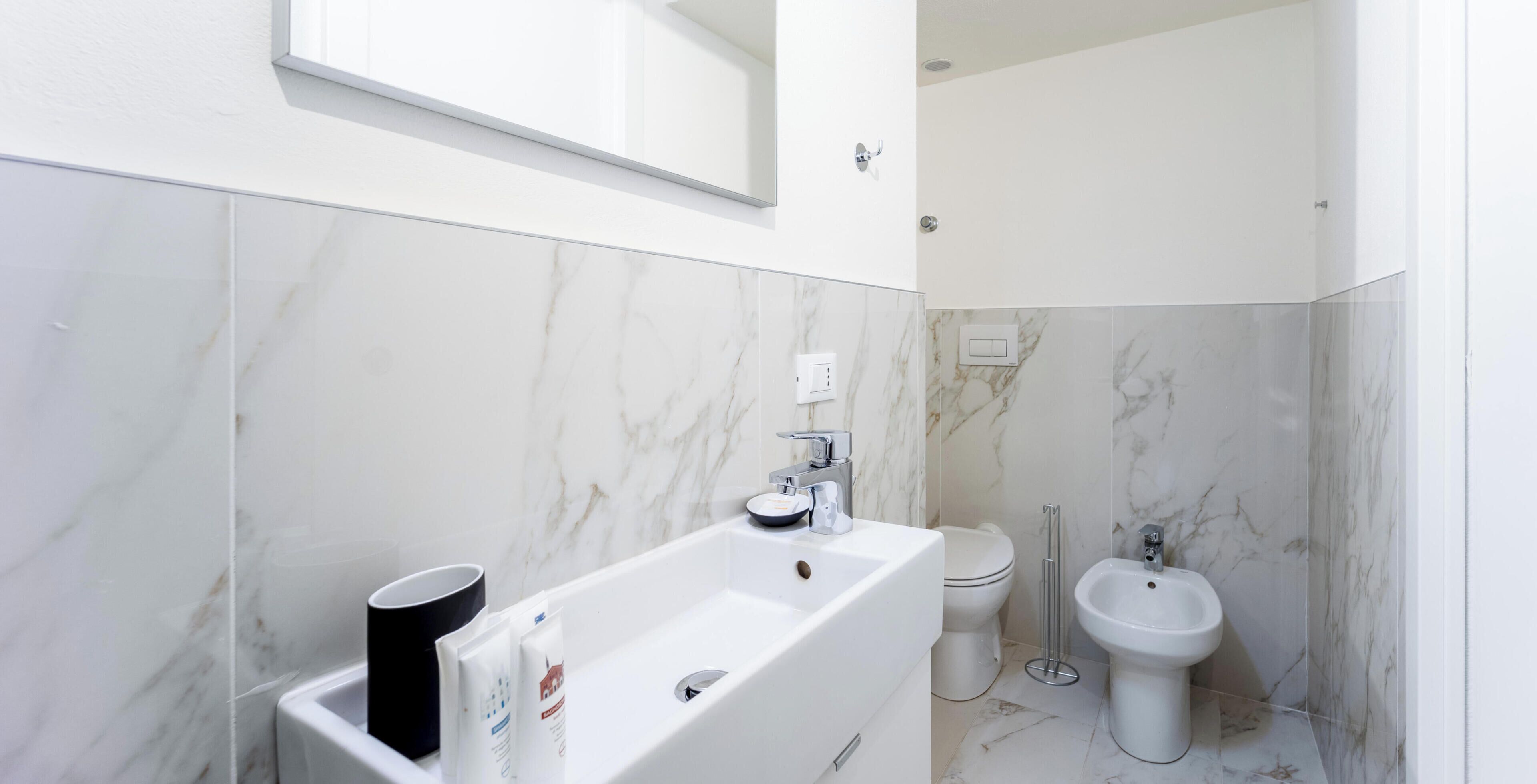 A modern bathroom with a white sink, mirror, and bidet.