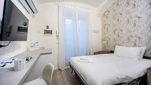 A hotel room with a bed, a desk with a chair, a TV, and a bathroom with a shower curtain. - Italianway - The B Village Standard - Apt T2 (Milan)