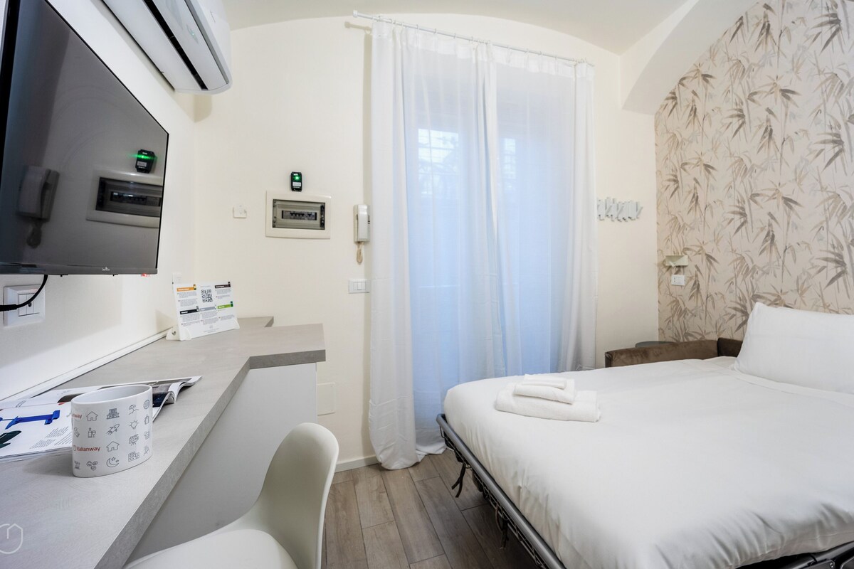 A hotel room with a bed, a desk with a chair, a TV, and a bathroom with a shower curtain.