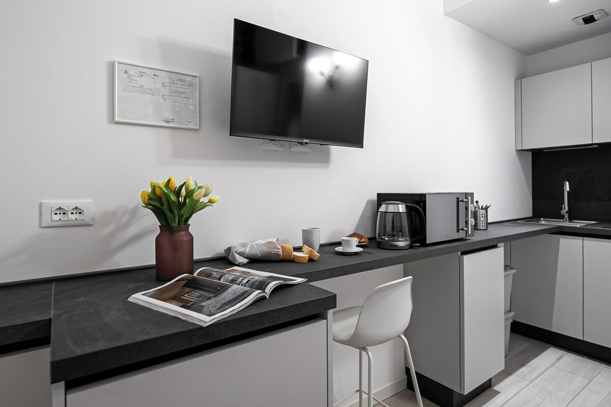 A modern kitchen with a flat-screen TV, a coffee maker, and a magazine on the counter.
