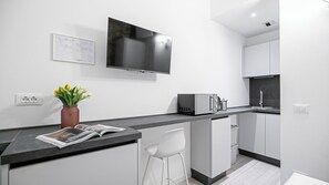 A modern kitchen with a flat-screen TV, a microwave, a sink, and a bar area with stools. - Italianway - The B Village Standard - Apt T2 (Milan)