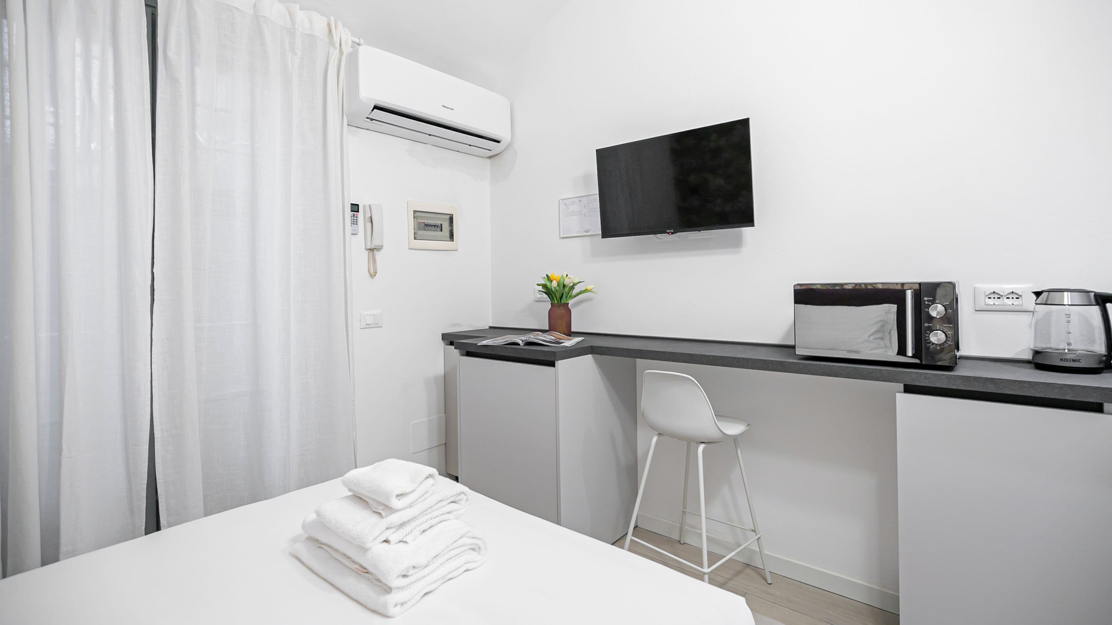A hotel room with a bed, a desk with a chair, a flat-screen TV, a coffee maker, and an air conditioner.