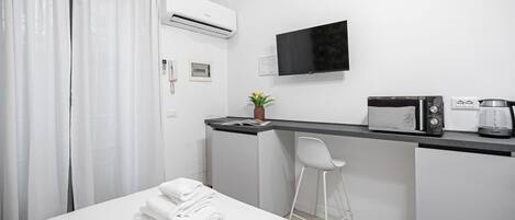 A hotel room with a bed, a desk with a chair, a flat-screen TV, a coffee maker, and an air conditioner.