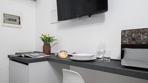 A modern kitchenette with a flat-screen TV, a small plant, a bread roll, a bowl, and a wine glass. - Italianway - The B Village Standard - Apt T2 (Milan)
