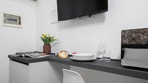 A modern kitchenette with a flat-screen TV, a small plant, a bread roll, a bowl, and a wine glass. - Italianway - The B Village Standard - Apt T2 (Milan)