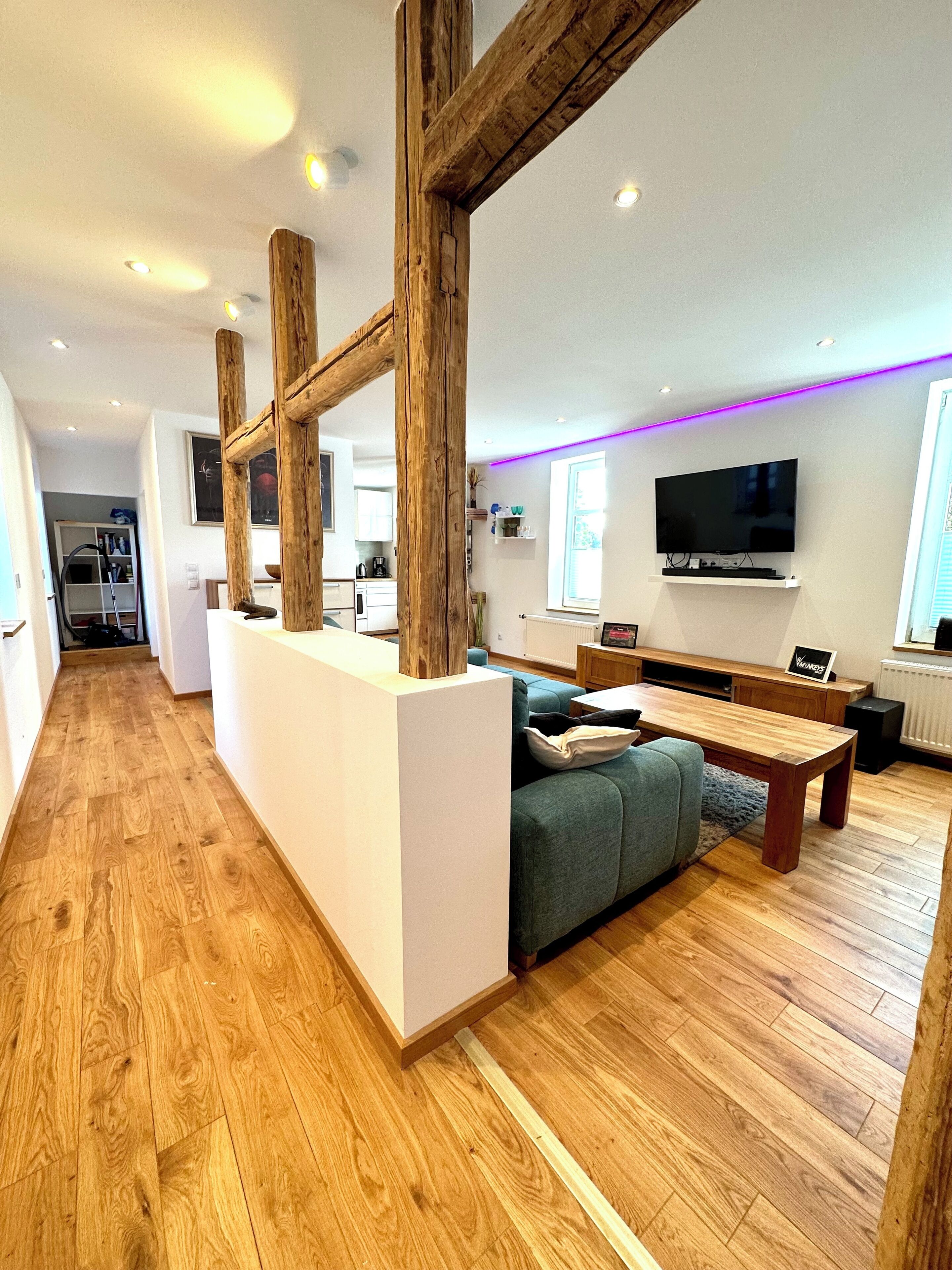 A modern living room with wooden flooring, a sofa, a coffee table, and a television mounted on the wall.