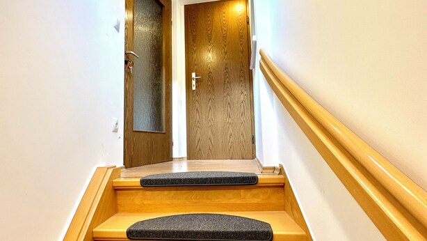 Una escalera con escalones de madera y peldaños antideslizantes negros, que conduce a una puerta con diseño de paneles de madera.