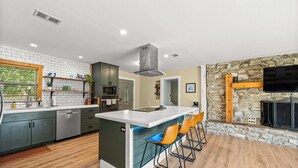Een moderne keuken met een centraal eiland, barstoelen, een stenen openhaard en een groot raam.
