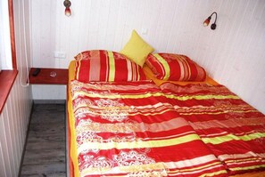 Ein Bett mit einer gestreiften roten und gelben Tagesdecke, ein einzelnes gelbes Kopfkissen und ein Nachttisch aus Holz mit einer Fernbedienung.