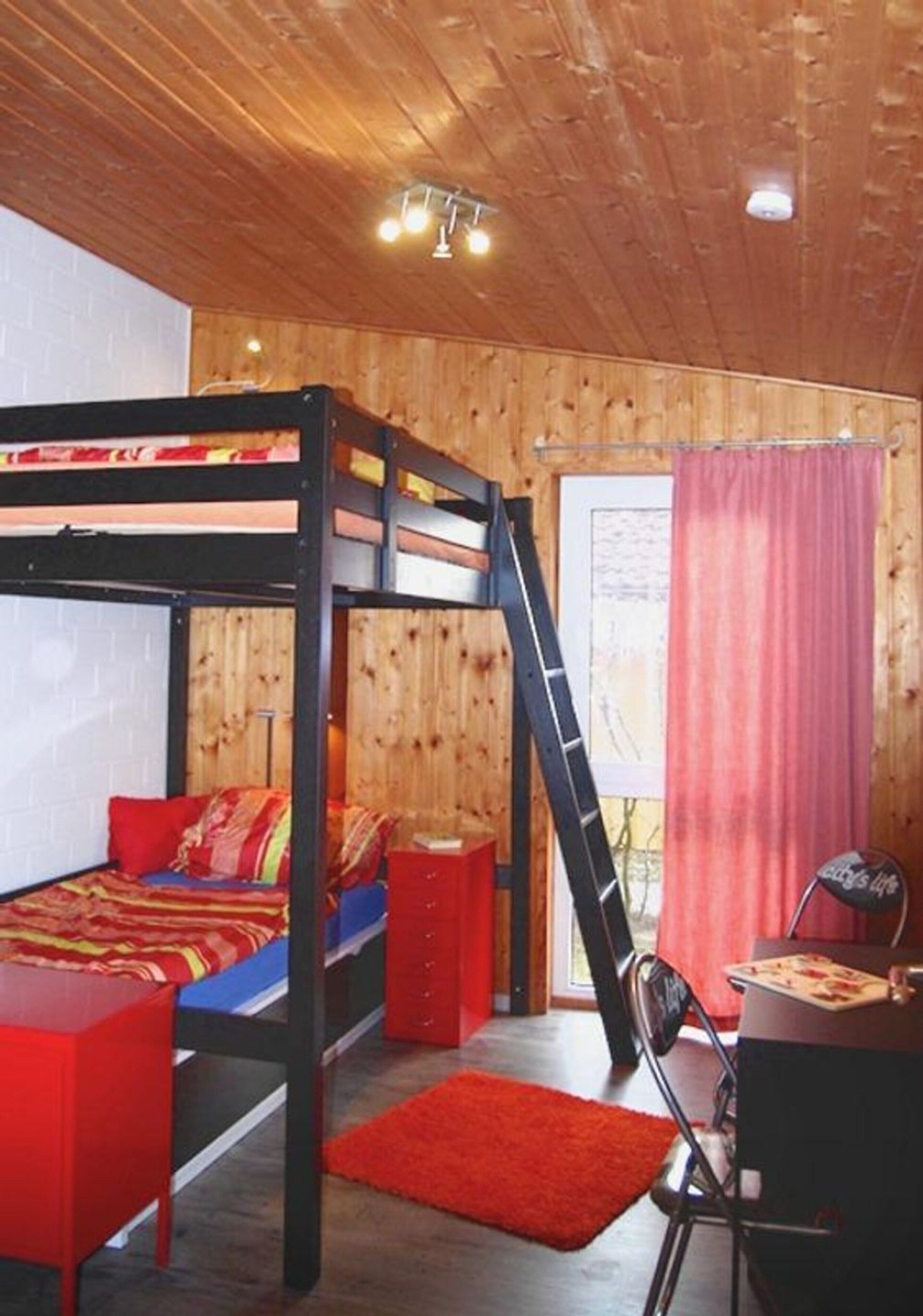 A bunk bed room with a desk and chair, wooden walls, and a red curtain.