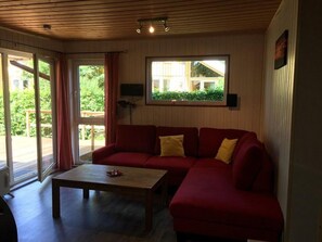 Ein Zimmer mit einem roten Sofa, einem Holztisch und einem Fenster mit Blick auf Grünflächen.