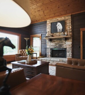 A cozy living room with a stone fireplace, leather furniture, and a large window.