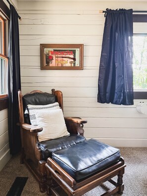 A wooden chair with a black cushion, a framed poster on the wall, and a window with a dark curtain. - Dutton Chapel Lodge (Golconda No. 2 Precinct)