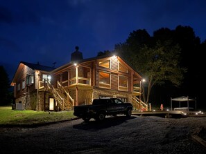 A two-story log cabin with a stone foundation, a covered porch, and a truck parked in front.
