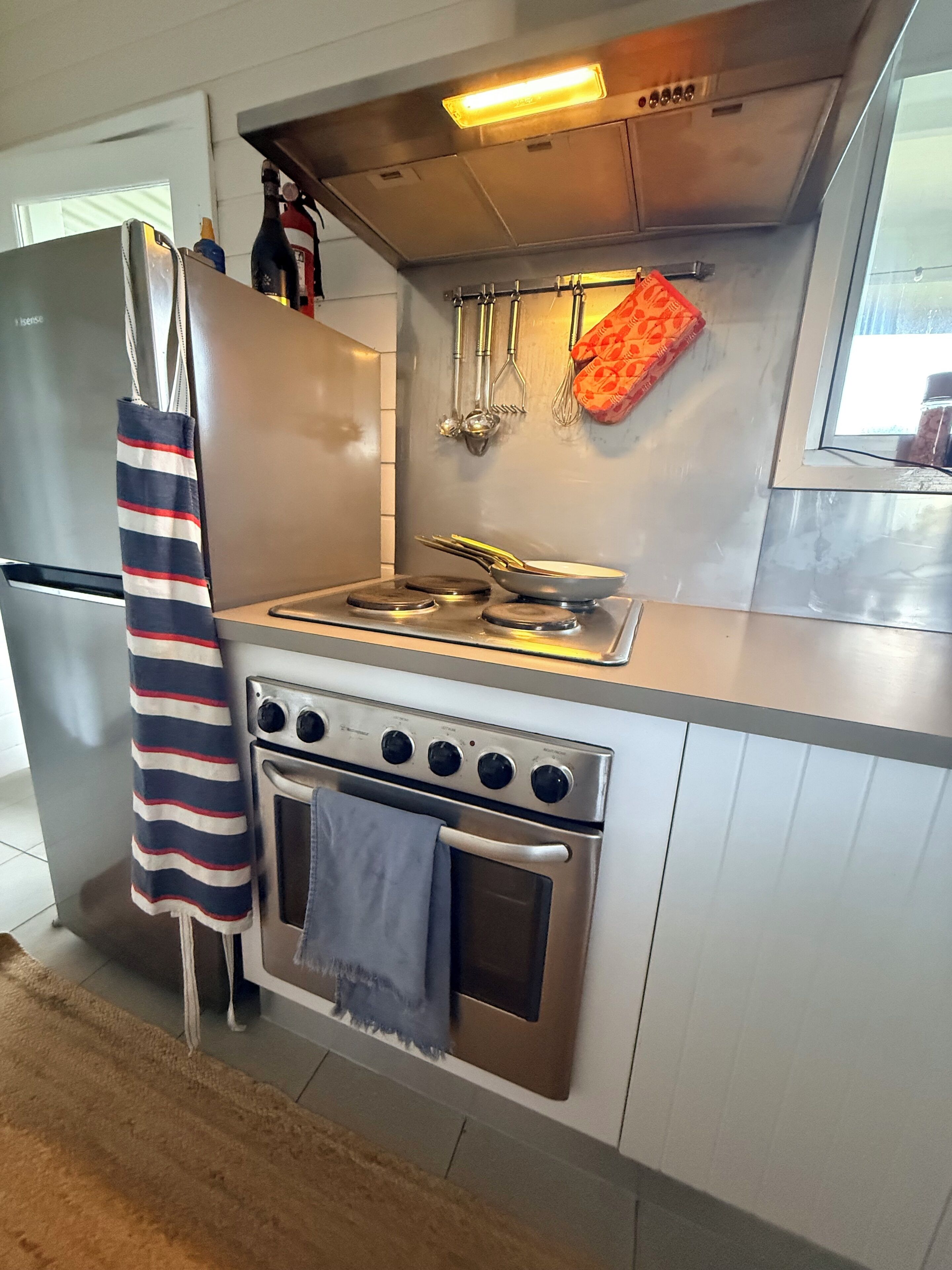 Una cocina con un refrigerador de acero inoxidable, una estufa a gas, un horno y utensilios de cocina colgando.