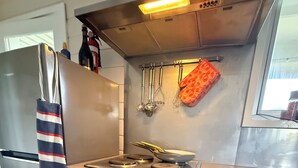Eine Küche mit Edelstahl-Kühlschrank, Gasherd, Backofen und abgehängten Küchenutensilien.