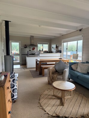 A modern kitchen with a central island, a dining area with a table and chairs, and a living room with a sofa and a coffee table. - Barlavento | A cosy beach shack that feels
like home | Long Beach Robe SA. (Robe)