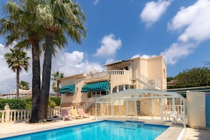 A pool area with a clear blue pool, palm trees, and a building with a balcony and outdoor seating. - Casa Nuestro Sueño for 6 People (Calpe / Calp)