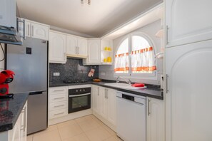 Una cuina moderna amb armaris blancs, un frigorífic d'acer inoxidable, un forn de sobre i un rentaplats.