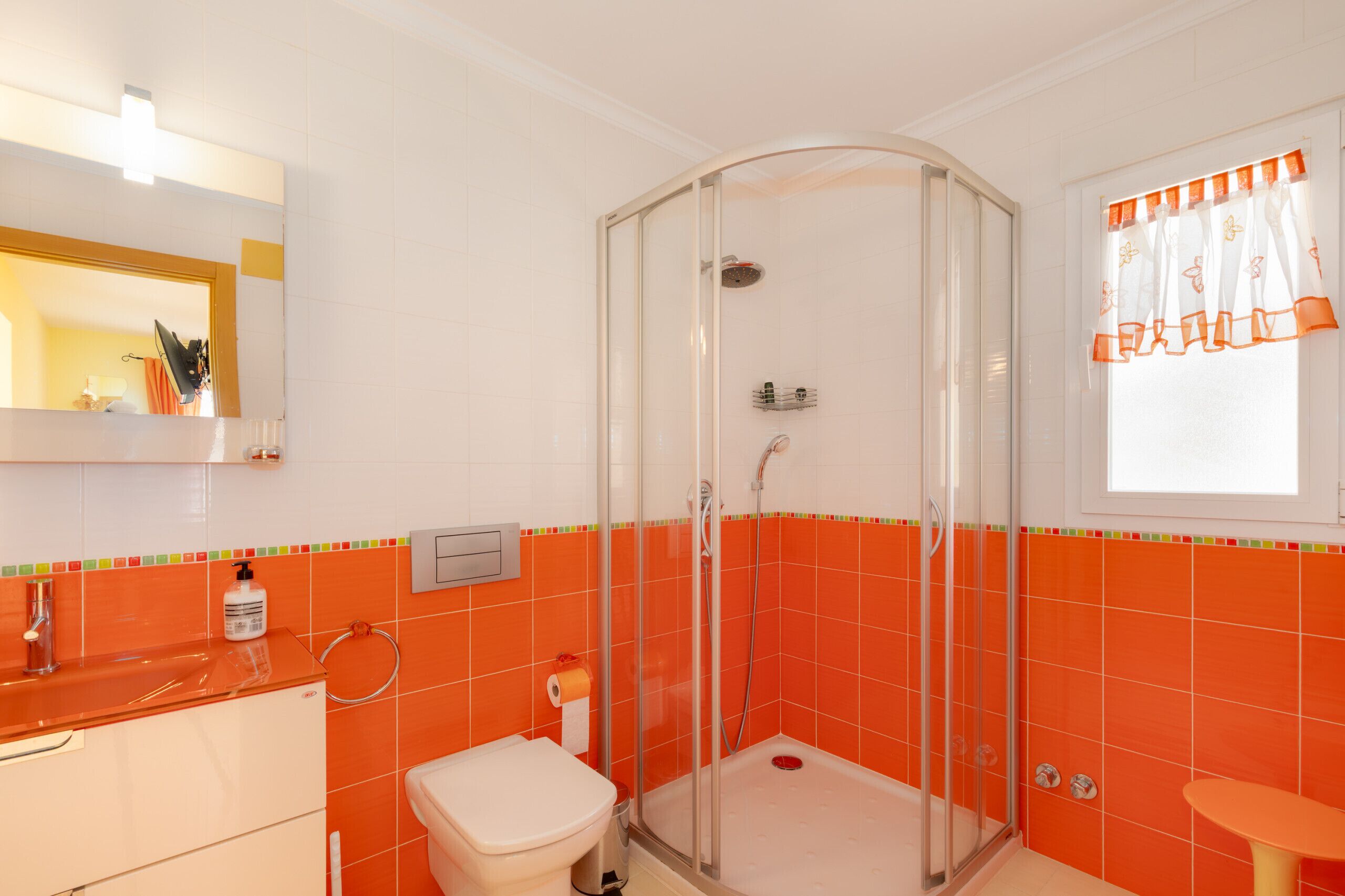 Une salle de bain avec une douche à parois de verre, des toilettes, un lavabo et une fenêtre avec des rideaux.