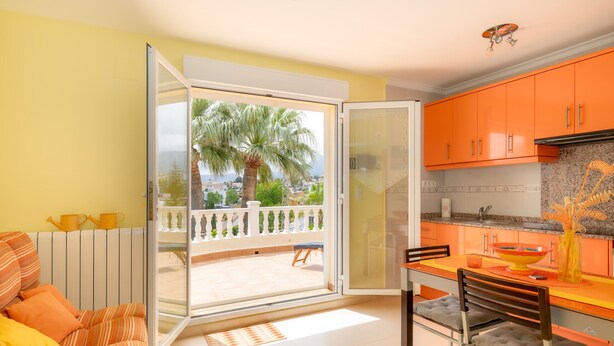 Ein Zimmer mit Balkon, Essbereich und orangenen Schränken.