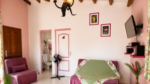 Una stanza con un letto, una scrivania, una sedia, una ventola, una TV e una porta che dà su un bagno.
