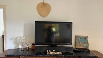 A flat-screen TV on a black stand with a 'Welcome' sign, a framed picture, and a vase with decorative items on a marble countertop.