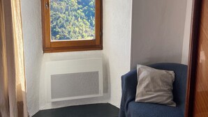 Una habitación de esquina con ventana, radiador, una silla azul y suelo de madera.