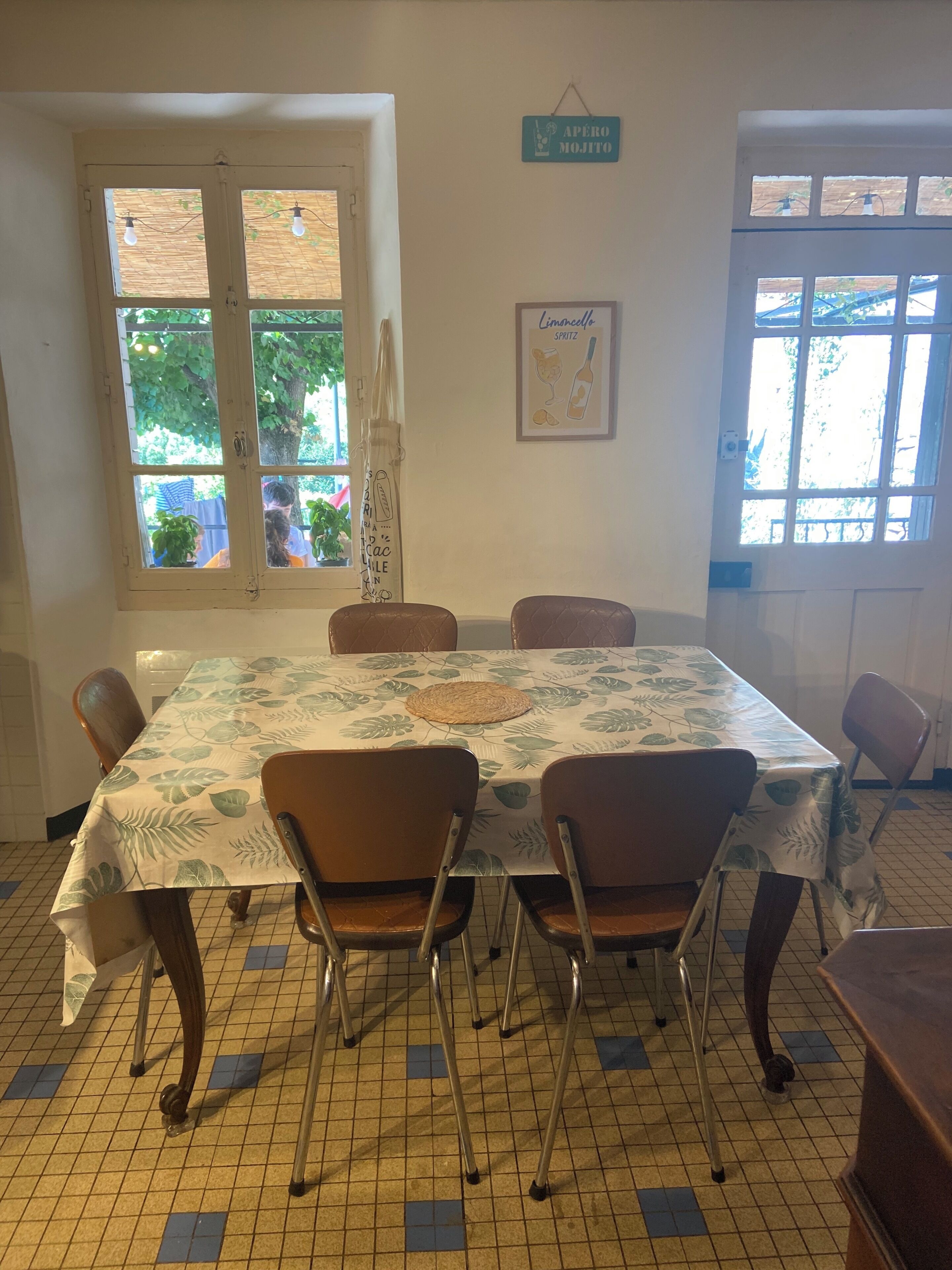 A dining area with a table covered in a leaf-patterned tablecloth, surrounded by chairs.
