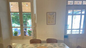 Un comedor con una mesa cubierta por un mantel estampado con hojas, rodeada de sillas.
