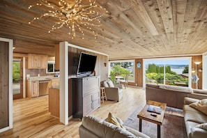 A spacious living area with a wooden ceiling, a television, and a view of a landscape. - Walk to Private Beach: Bay-View Whidbey Island Gem (Oak Harbor)
