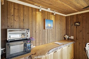 A kitchen with wooden walls, a microwave, a toaster, and a small table with a vase of flowers. - Walk to Private Beach: Bay-View Whidbey Island Gem (Oak Harbor)
