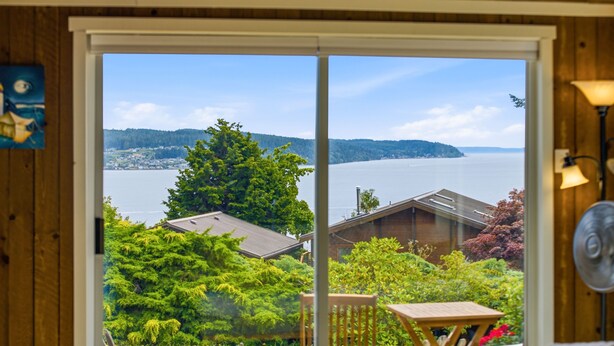 Una habitación con un amplio ventanal corredera que da a vistas de un lago, rodeado de vegetación y una terraza de madera.