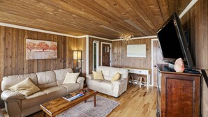 Un salón acogedor con paredes de madera, un sofá, un sillón adicional, una mesa de centro y un televisor de pantalla plana.