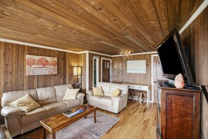 Ein gemütliches Wohnzimmer mit Holzwänden, einer Couch, einem kleinen Sofa, einem Couchtisch und einem Flachbildfernseher.