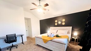 Un dormitorio con cama, escritorio, ventilador de techo, mesita de noche y lámpara.