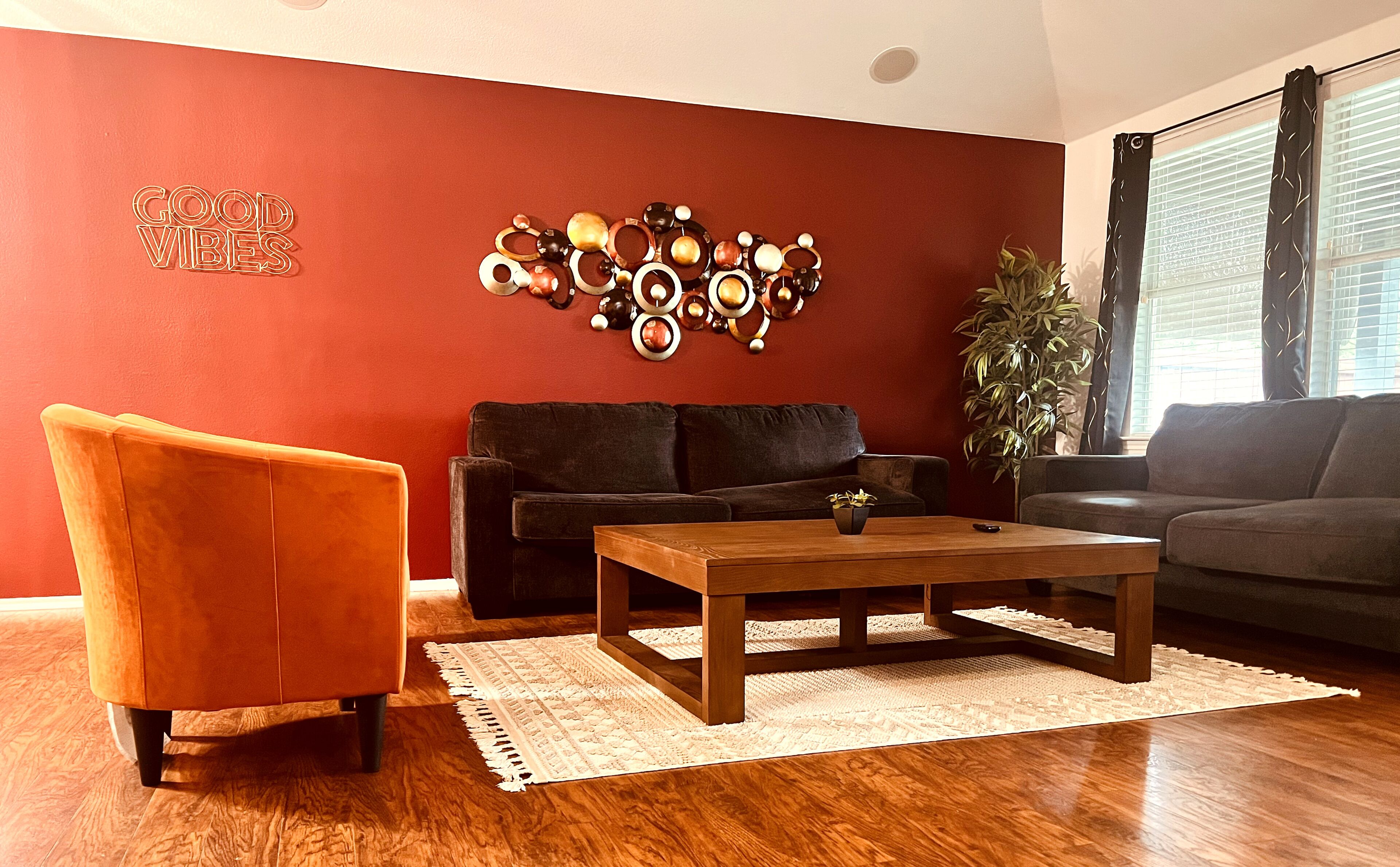 A living room with a red accent wall, a black sofa, an orange armchair, a wooden coffee table, and a decorative wall piece.