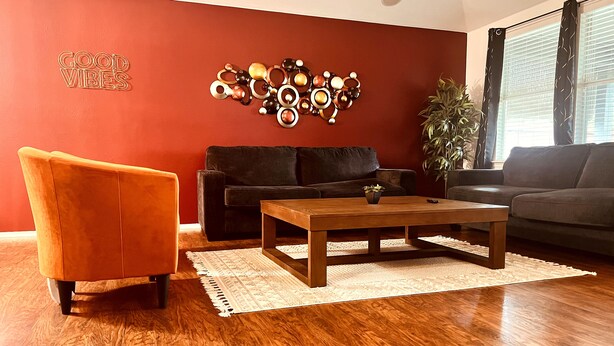 Sala de estar con una pared de acento roja, un sofá negro, un sillón naranja, una mesa de centro de madera y un elemento decorativo en la pared.