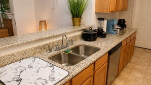 Cocina con encimeras de granito, pileta de acero inoxidable, muebles de madera y electrodomésticos modernos, incluyendo cafetera y licuadora.