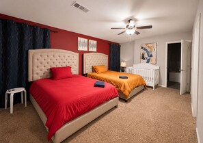 A bedroom with two beds, a ceiling fan, and a door leading to a bathroom.