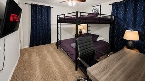 Quarto com beliche, ventilador de teto, televisão na parede e escrivaninha com luminária.