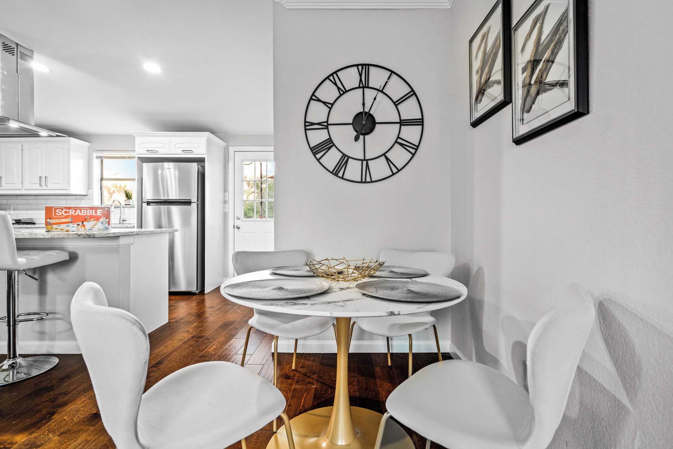Una cocina moderna con armarios blancos, un refrigerador de acero inoxidable y un comedor con una mesa redonda y sillas blancas.