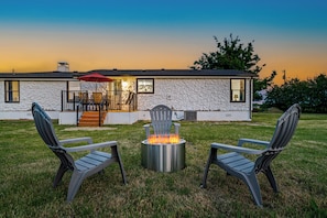 Uma casa de pedra com uma lareira e duas cadeiras Adirondack no jardim.