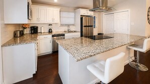 Uma cozinha moderna com armários brancos, bancada de granito, eletrodomésticos de aço inoxidável e um espaço de bar com banquetas.